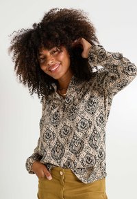 Blusa beige con patrones florales y de cachemira en negro, con mangas largas y cuello abotonado. Tejido texturizado con un corte relajado.