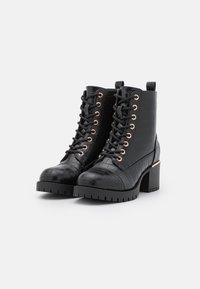 Černé kotníkové boty s krokodýlím vzorem, šněrování v přední části, chunky podpatky a zlaté očko, zobrazené na bílém pozadí.