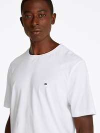 White cotton T-shirt with short sleeves, featuring a small logo on the chest. The fabric appears smooth and lightweight.