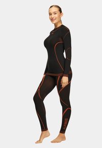 Czarny zestaw odzieży sportowej z długimi rękawami i legginsami, z pomarańczowymi akcentami, teksturowanym materiałem i dopasowanym krojem.