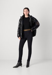 Doudoune noire avec finition brillante, haut noir ajusté, ceinture à imprimé léopard, pantalon noir sur mesure et bottines noires à talons pointus.