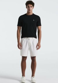 Zwarte korte mouwen t-shirt, geribbelde textuur, met klein logo; witte shorts, iets losse fit, gladde stof, gecombineerd met witte sneakers.