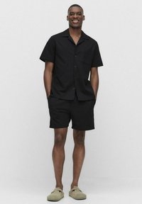 Zwarte T-shirt met korte mouwen en een zak, gecombineerd met bijpassende zwarte shorts. Zachte textuur, eenvoudig ontwerp. Lichtgekleurde instappers.