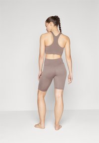 Reggiseno sportivo marrone e pantaloni corti a vita alta in materiale elasticizzato. Il design presenta uno scollo a dorso nudo e una costruzione senza cuciture.