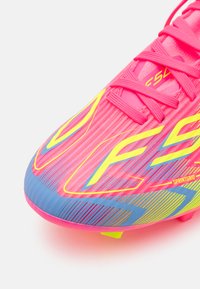 Lys rosa fotballsko med gule og blå grafiske detaljer, rosa lisser og teksturert overflate.