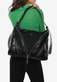 Sac à main en cuir noir au design angulaire, avec plusieurs poches zippées, des accents de bracelet cloutés et une finition brillante.