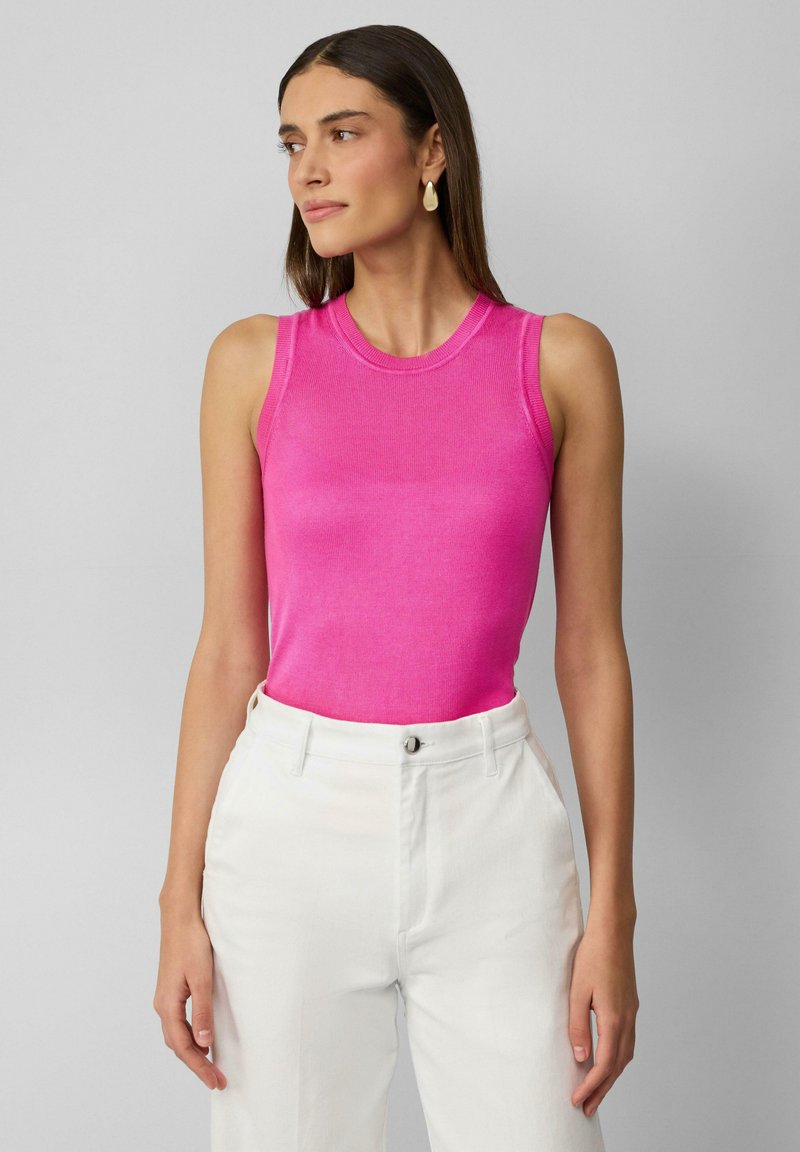 Dopasowany bezrękawnik w jasnoróżowym prążkowanym materiale, w zestawie z białymi spodniami z wysokim stanem z detalem w postaci guzika. Prosty, nowoczesny design.