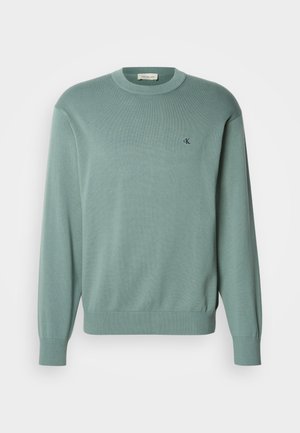 Svetlozelený pletený sveter s okrúhlym výstrihom, dlhými rukávmi a rebrovanými manžetami. Na hrudi má malý logo. Textúra pôsobí mäkko.