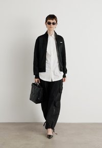 Black zip-up jacket, white button-up shirt, black cargo pants, black heeled shoes, and a textured black handbag. Accessories include sunglasses.