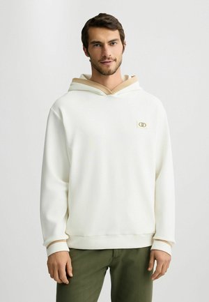 Sudadera blanca con un acento beige en la capucha. Presenta un pequeño logo en el pecho, mangas largas y un diseño de corte relajado.