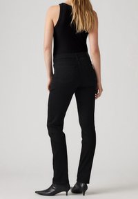 Jeans negros con un diseño ajustado, que presentan una cintura de altura media. Dos bolsillos traseros con un sutil detalle de logo. Textura de denim suave, sin patrones visibles.