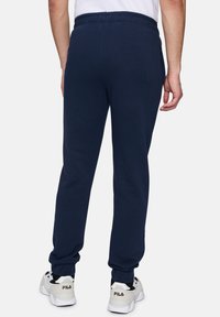 Marineblauwe sweatpants met een aansluitende boord, elastische tailleband en zijzakken, gecombineerd met zwart-witte sportschoenen.