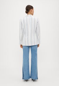 White blazer with vertical blue stripes, tailored design, and notched lapels, paired with light blue flared jeans. Smooth texture throughout.