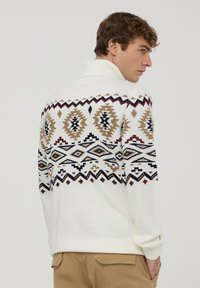 Kremowy sweter z dzianiny z wysokim kołnierzem, zdobiony kolorowym geometrycznym wzorem w brązie, czerni i burgundzie na plecach.