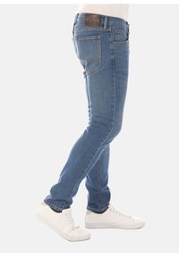 Tajta blå jeans i denim med femfickorsdesign, ton-i-ton sömmar och en läderlogotyp på baksidan av midjan. Bärs med vita sneakers.