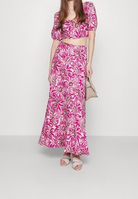 Kaksiosainen asu, joka koostuu lyhyestä topista puffiolkaimilla ja pitkästä hameesta, molemmat vaaleanpunaisessa kukkakuosissa kermanvärisellä taustalla.