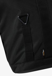 Svart Cordura nylonbag med teksturert overflate, justerbare stropper i vevd bånd og en trekantet metallpynt.