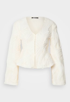 Balta garām piedurknēm topi ar teksturētu spirāli, V-veida kakla izgriezumu un pogu aizdari. Mīksts materiāls ar pieguļošu vidukli un izvērstām piedurknēm.