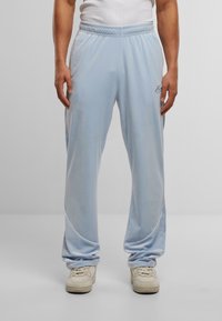 Pantaloni da tuta velour azzurro chiaro con vita elasticizzata, piping bianco lungo i lati e un piccolo logo ricamato davanti.
