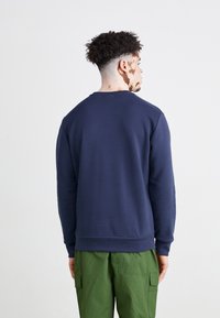 Sweatshirt din bumbac de culoare bleumarin, cu decolteu rotund și tiv ribbit; modelat cu pantaloni cargo verzi pe un fundal alb simplu.