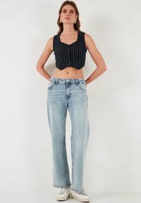 Jūras spēku svītrains īsais tops ar priekšējiem pogām, kombinēts ar gaiši ziliem platajiem džinsiem. Modelis valkā baltas kedas. Vienkārša fona.