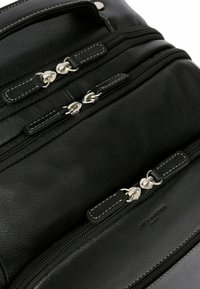 Zaino in pelle nera con più scomparti con zip, dotato di accessori in metallo argentato e cuciture bianche a contrasto sulle zip e sulle chiusure.