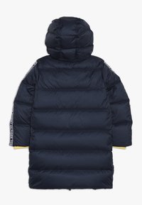 Námořnická puffer bunda s kapucí, horizontálním prošíváním a žlutými akcenty na manžetách. Obsahuje značkové pruhy podél rukávů. Hladká textura.