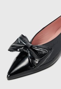 Ballerines noires en cuir verni à bout pointu présentant un grand nœud décoratif sur le devant et une doublure intérieure rose douce. Texture lisse sur l'ensemble.