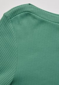 Tissu vert à côtes avec une texture lisse, arborant un col rond et un détail sur l'épaule. La couleur est uniforme sur l'ensemble de la pièce.