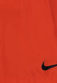 Pantalones cortos de tela roja con una textura suave, presentando un logo de Nike negro en la parte inferior izquierda. Diseño simple sin patrones adicionales.