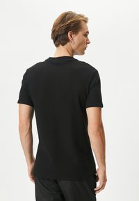 Camisa negra de manga corta en tejido texturizado con cuello redondo y corte relajado. Presenta un patrón sutil y un diseño minimalista.