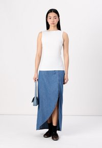 Weißes ärmelloses Oberteil, Denim-Maxi-Rock mit seitlichem Schlitz, schwarze Socken und Schuhe mit Leopardenmuster. Blauer Handtasche als Accessoire.