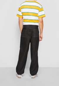 Avslappnad randig t-shirt i vitt, gult och turkosa, tillsammans med högmidjade svarta jeans med två bakfickor.