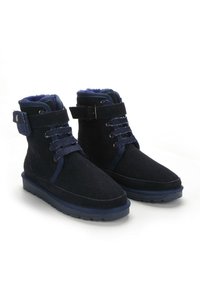 Botas de tobillo de ante azul marino con un suave forro interior, cordones en la parte delantera, tiras ajustables y suela de goma texturizada.