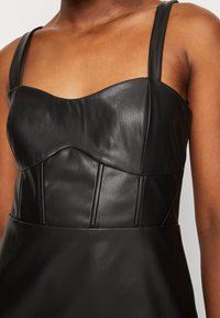 Robe en cuir noir avec un corsage ajusté à encolure arrondie, larges bretelles, coutures verticales et texture lisse.