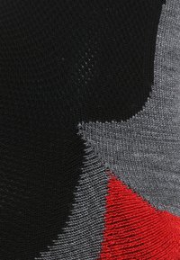 Tejido de punto con un atrevido diseño abstracto en negro, gris y rojo, con texturas variadas y transiciones de color suaves e interconectadas.