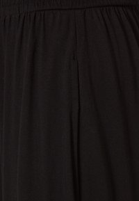 Tissu noir avec une texture douce, présentant des plis sur le devant. La taille élastique offre flexibilité et confort.