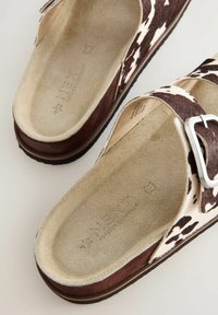 Bruna och vita sandaler med cow-print i mjukt mocka, med en bred rem och en silverfärgad spänne. Texturerade inlägg för komfort.