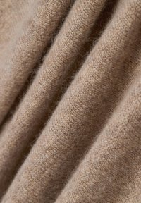 Beige kasjmier stof met een zachte, gestructureerde oppervlakte, met plooien die de warmte en dikte benadrukken.
