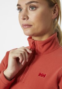 Rode fleece pullover met een hoge kraag en een halve rits. Bevat een klein geborduurd logo op de borst en heeft een zachte textuur.