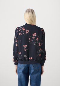 Felpa a motivi floreali in blu navy con fiori rosa e verdi. Polsini e orlo a coste, vestibilità comoda, tessuto morbido. Abbinata a jeans blu.