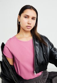 Lys rosa kortermet skjorte med rund halslinning, sammen med en svart skinn bomberjakke med cropped passform, som har sølvglidelås og ribbestrikkede mansjetter.