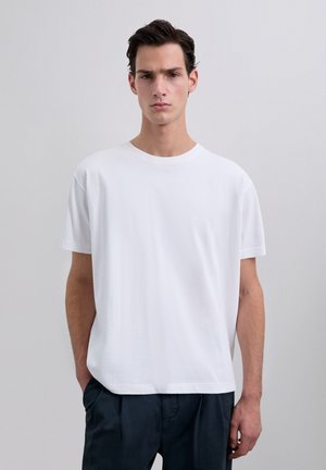 White crew-neck t-shirt made of smooth cotton; relaxed fit; short sleeves; no graphics or patterns; paired with dark pants.