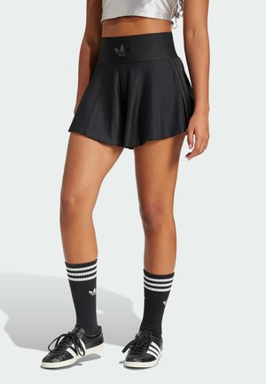 Frau trägt schwarze Adidas Schlagshorts, schwarze Adidas Kurzsocken mit weißen Streifen und schwarze Adidas Sneaker mit weißen Streifen.
