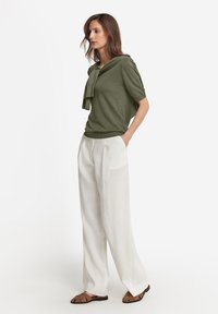 Olivgrön kortärmad tröja med draperad detalj, kombinerad med vita vida byxor och bruna platta sandaler. Slät textur, avslappnad passform.