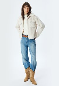 Cremefarvet faux fur jakke med to brystlommer, parret med lyseblå straight-leg jeans og brune cowboystøvler med broderede detaljer.