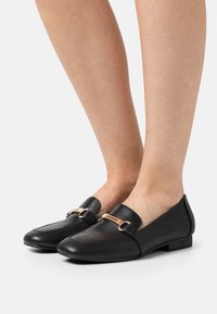 Černé loafers vyrobené z hladké kůže, s nízkým podpatkem a zlatým akcentem na přední straně, s jednoduchým designem.