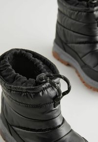 Bottes isolées noires avec tige matelassée, haut élastiqué et semelle en caoutchouc grise. Comprend une languette et un cordon de serrage pour un ajustement sécurisé.