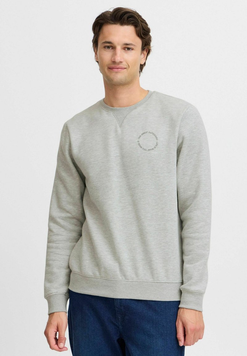 Sudadera gris claro con cuello redondo y puños acanalados. Presenta un logo en gris oscuro en el pecho. Tejido suave con un ajuste casual.