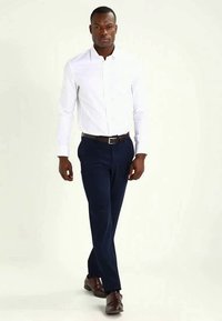Vit button-up skjorta, marinblå byxor, bruna läderskor. Enkelt mönster och skräddarsydd passform. Inga synliga mönster; slät textur.